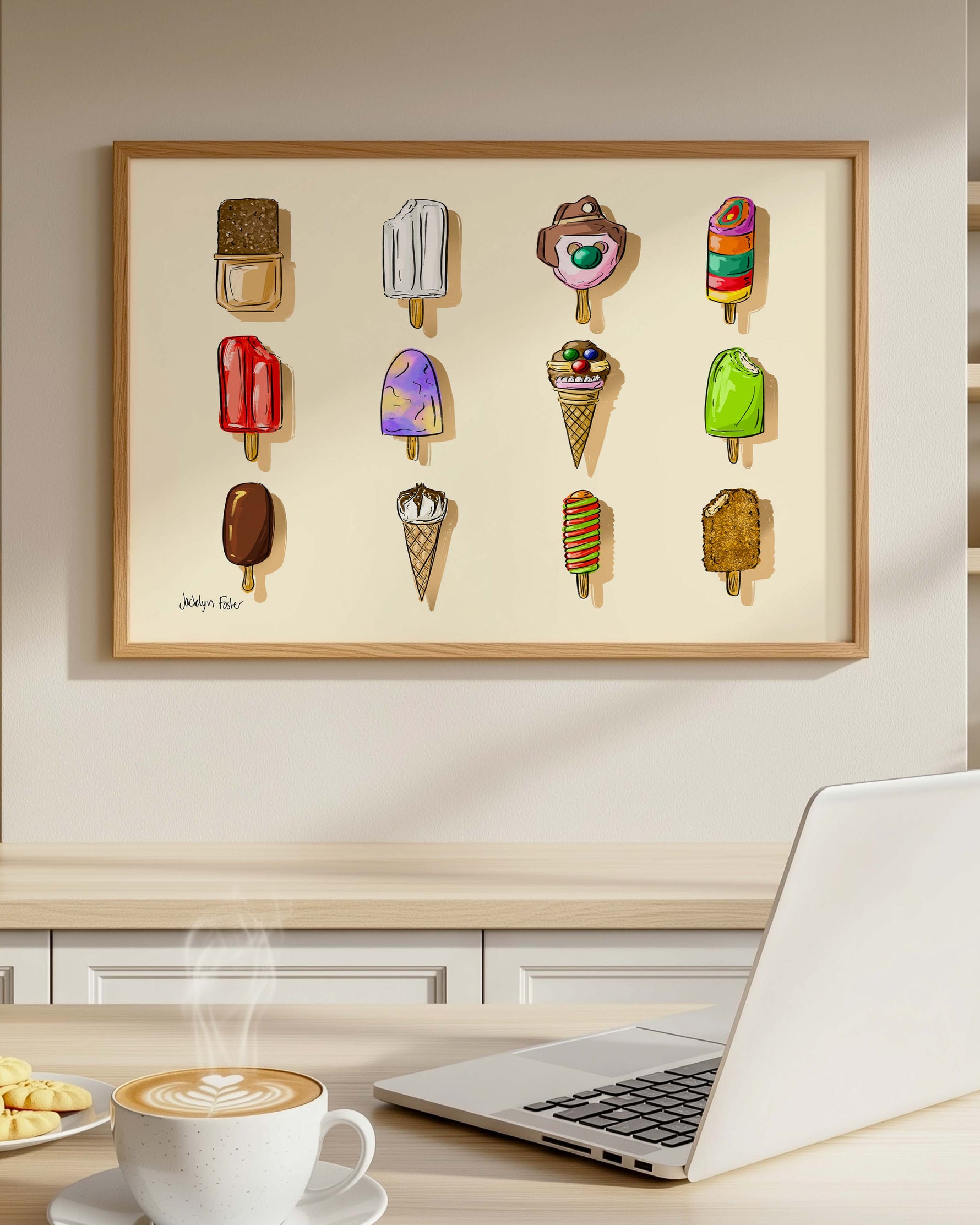 Laptop on a desk with a cup of coffee, cookies, and a wall art of ice cream cones and popsicles in a kitchen setting.